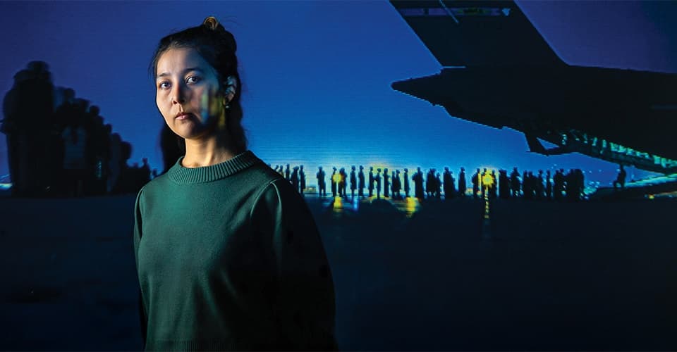 portrait of Fatema Hosseini in front of a projected image of Afghans lining up to board a military jet