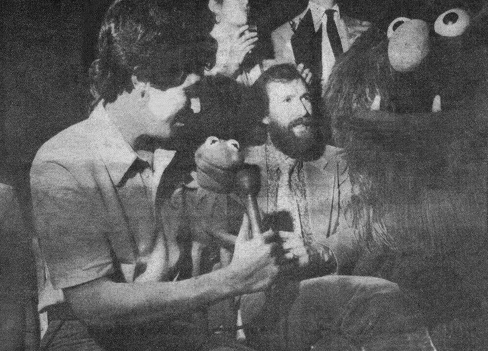 Reporter holds microphone to Kermit, held by Jim Henson