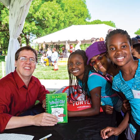 Jeff Kinney poses with kids as he signs their copy of "Diary of a Wimpy Kid" book