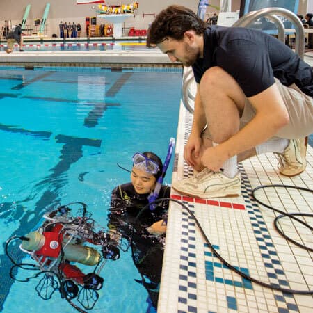 student and diver watch underwater robot in pool